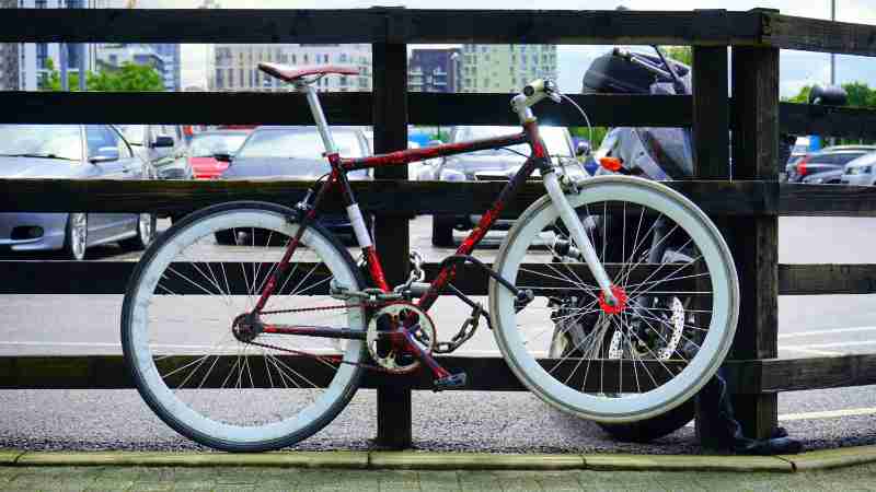 A vibrant bicycle locked to a wooden railing in a city parking lot with background cars., tags: te met en - pexel