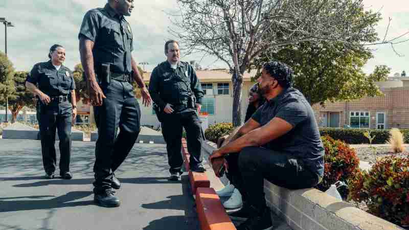 Police officers interacting with individuals seated outdoors in a parking area., tags: appartementinbraken - pexel