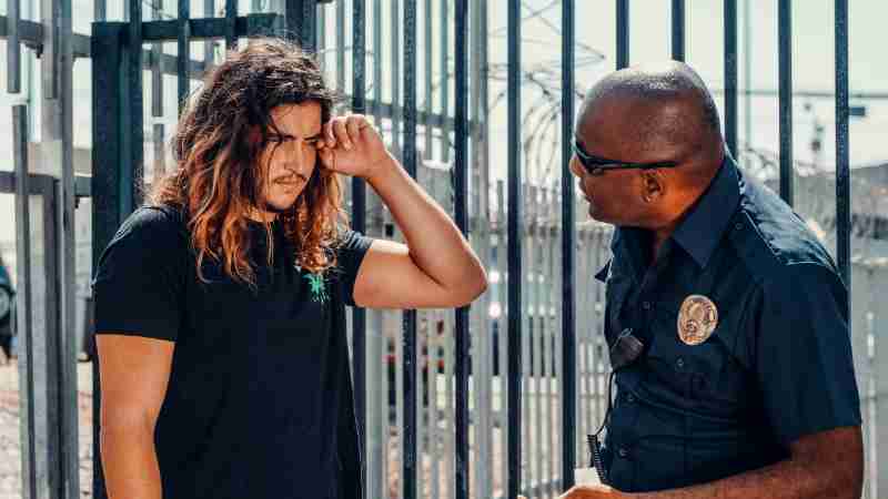 A police officer engages in a serious conversation with a civilian outdoors near a fence., tags: bewoners om te melden inbraken - pexel